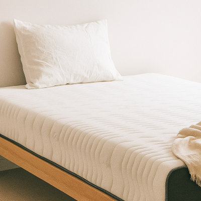 這張圖片展示了一間明亮簡約的臥室。主題是放在淺色木質懸浮床架上的「奶凍捲床墊」。床墊表面呈現白色波浪紋路,側邊則是深灰色的布料。